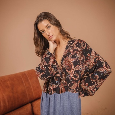 Blusa feminina com padrão paisley colorido sobre tecido azul claro, modelo posando em ambiente interior