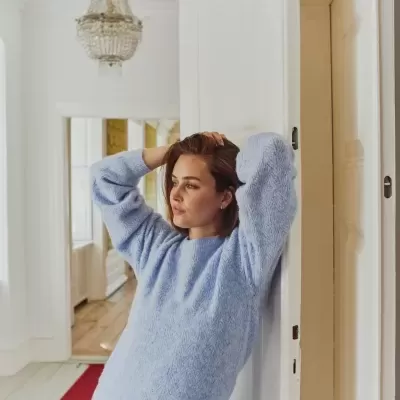 Mulher a usar suéter azul claro de malha felpuda com padrão e calças de ganga azuis num interior