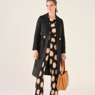 Mulher com casaco preto, roupas com padrão de círculos bege e mala camel