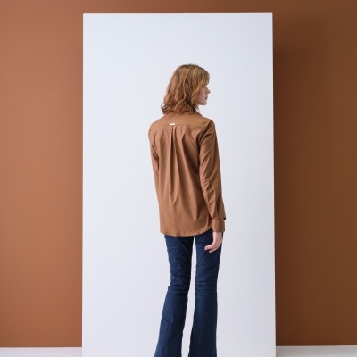 Pessoa de costas com camisa castanha de manga comprida e calças jeans azuis flare