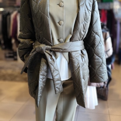 Manequim com casaco acolchoado verde-oliva com cinto, colete bege e camisa branca