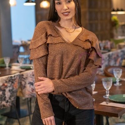 Mulher com túnica castanha brilhante e folhos nos ombros, calças pretas, em restaurante