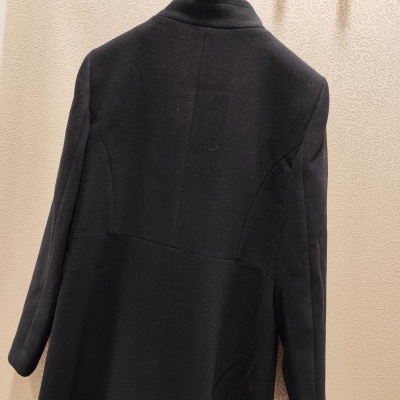 Casaco preto pendurado na parede com padrão decorativo creme