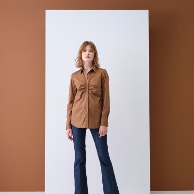 Mulher vestindo camisola castanha com franzido e calças de ganga azuis escuras