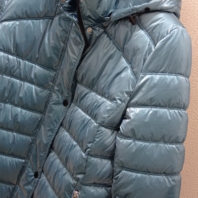 Casaco acolchoado verde-azulado com capuz e fecho de correr preto pendurado num cabide