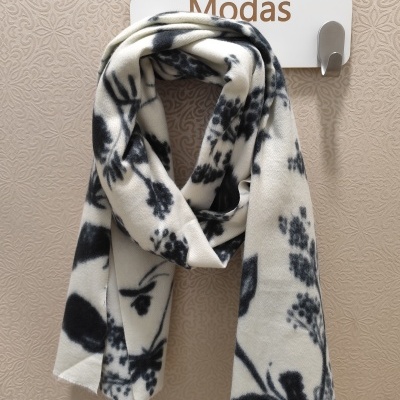 Cachecol branco com padrão floral preto pendurado num cabide branco com gancho metálico