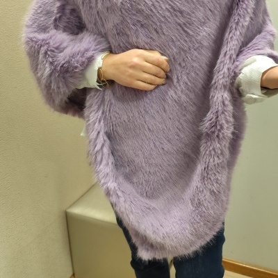 Poncho lilás peludo com gola alta usado por pessoa dentro de casa.