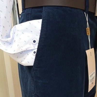 Calças de veludo azul-marinho com cinto castanho e camisa branca com padrão azul