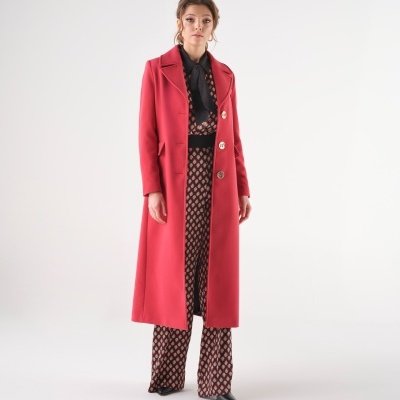 Mulher com casaco vermelho comprido e calças padrão geométrico em fundo branco