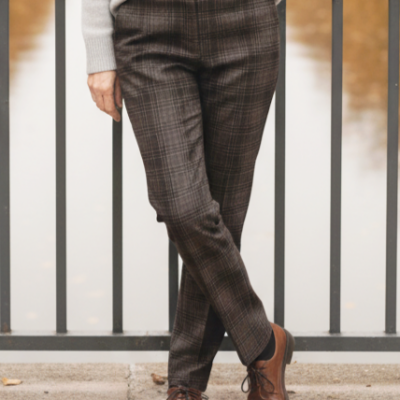 Pantalonas xadrez castanho e cinzento com casaco bege e sapatos castanhos ao ar livre junto a barreira metálica