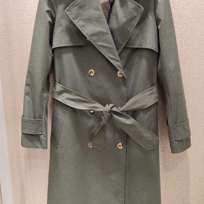 casaco trench coat verde com botões dourados suspenso em cabide