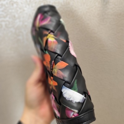 Mala preta com padrão floral entrelaçada sendo segurada à mão