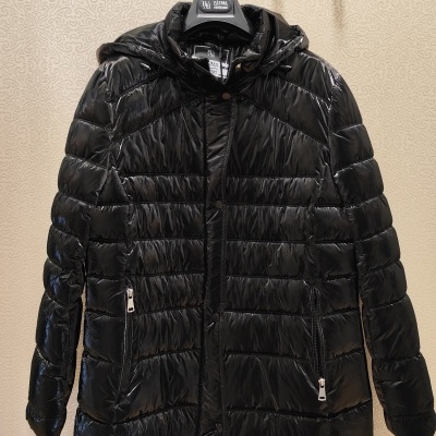 Casaco preto acolchoado brilhante com capuz pendurado com etiqueta em fundo texturizado e placa Prince Modas