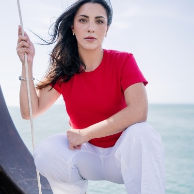 Mulher com t-shirt vermelha e calças brancas sentada numa embarcação junto ao mar