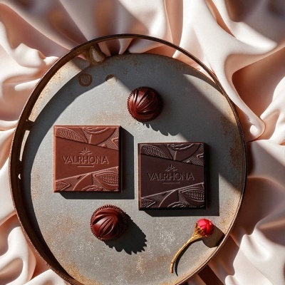 Chocolate Valrhona ao leite e negro com bombons em prato metálico sobre tecido rosa claro