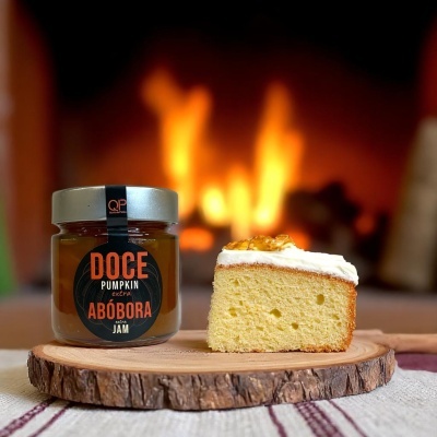 Frasco de doce de abóbora e fatia de bolo com cobertura sobre tábua de madeira com fogo ao fundo