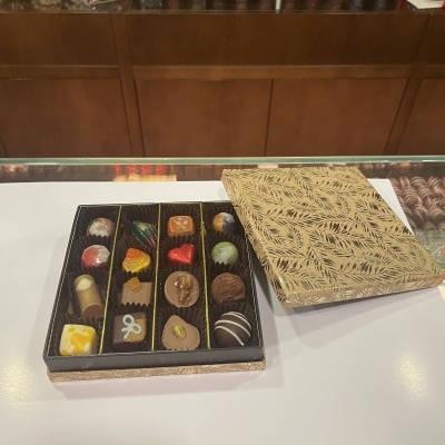 Caixa de bombons variados em caixa dourada com padrão de folhas sobre bancada branca