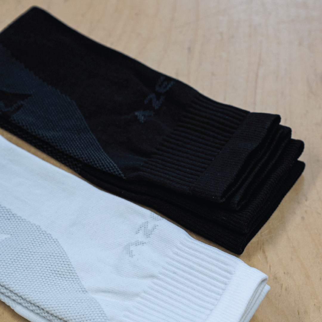 Dois pares de meias desportivas, uma preta outra branca, sobre madeira