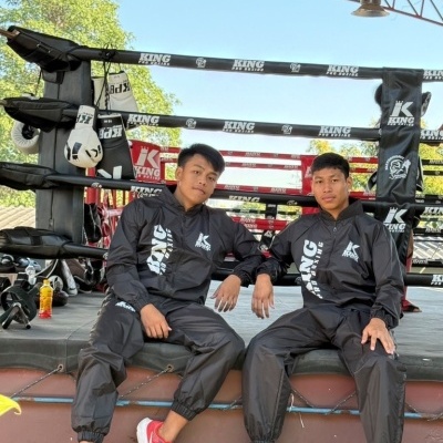 Dois homens com fatos de treino pretos junto a um ringue de boxe