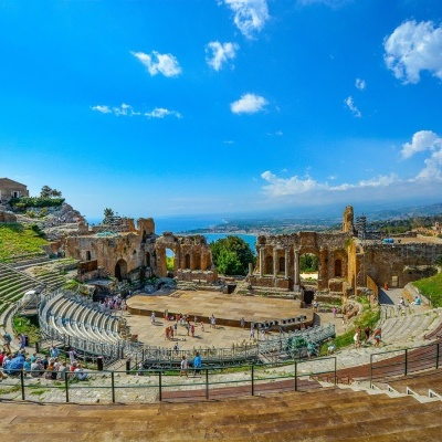 Anfiteatro antigo ao ar livre com bancos de pedra e ruínas sob céu azul