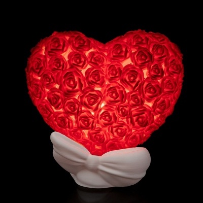 Coração decorativo vermelho de rosas iluminadas numa base branca com nó