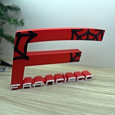 Objeto decorativo vermelho em forma de letra F com aranha preta e palavra FRANCISCO em branco
