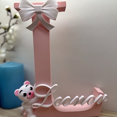 Letra decorativa cor-de-rosa com laço branco, urso, e nome Leonor em branco