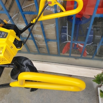 Máquina agrícola com punhos amarelos e corpo preto e amarelo, em chão de cimento diante de porta de vidro com grade azul