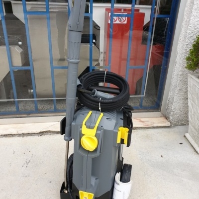 Máquina de lavar cinzenta com detalhes amarelos e mangueira enrolada junto a uma grade azul