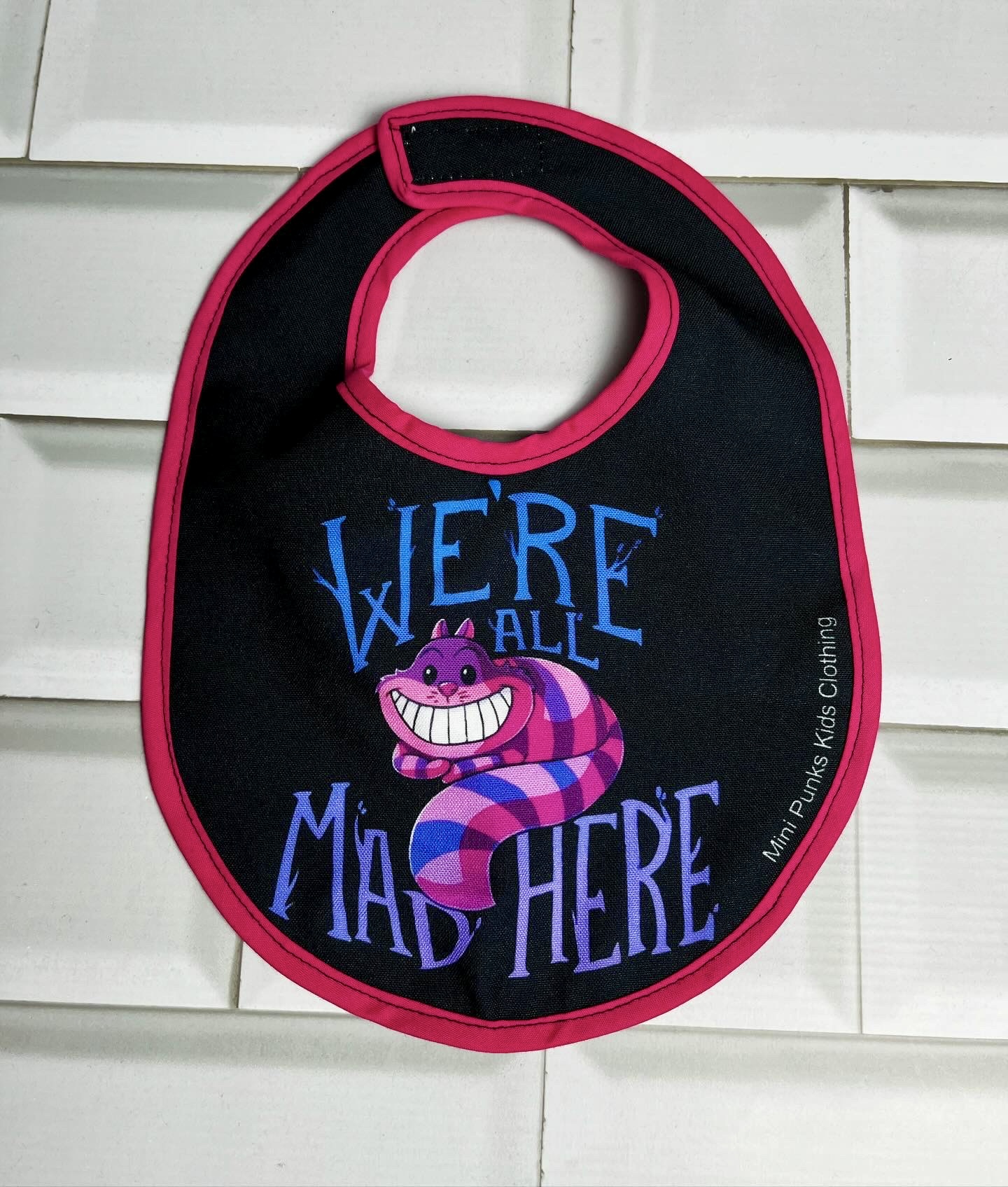 Babete preto com bordadura rosa e ilustração colorida do gato Risonho e texto azul