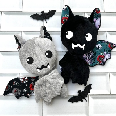 Peluches morcego cinza e preto com padrões coloridos nas asas e morcegos pequenos pretos na parede branca