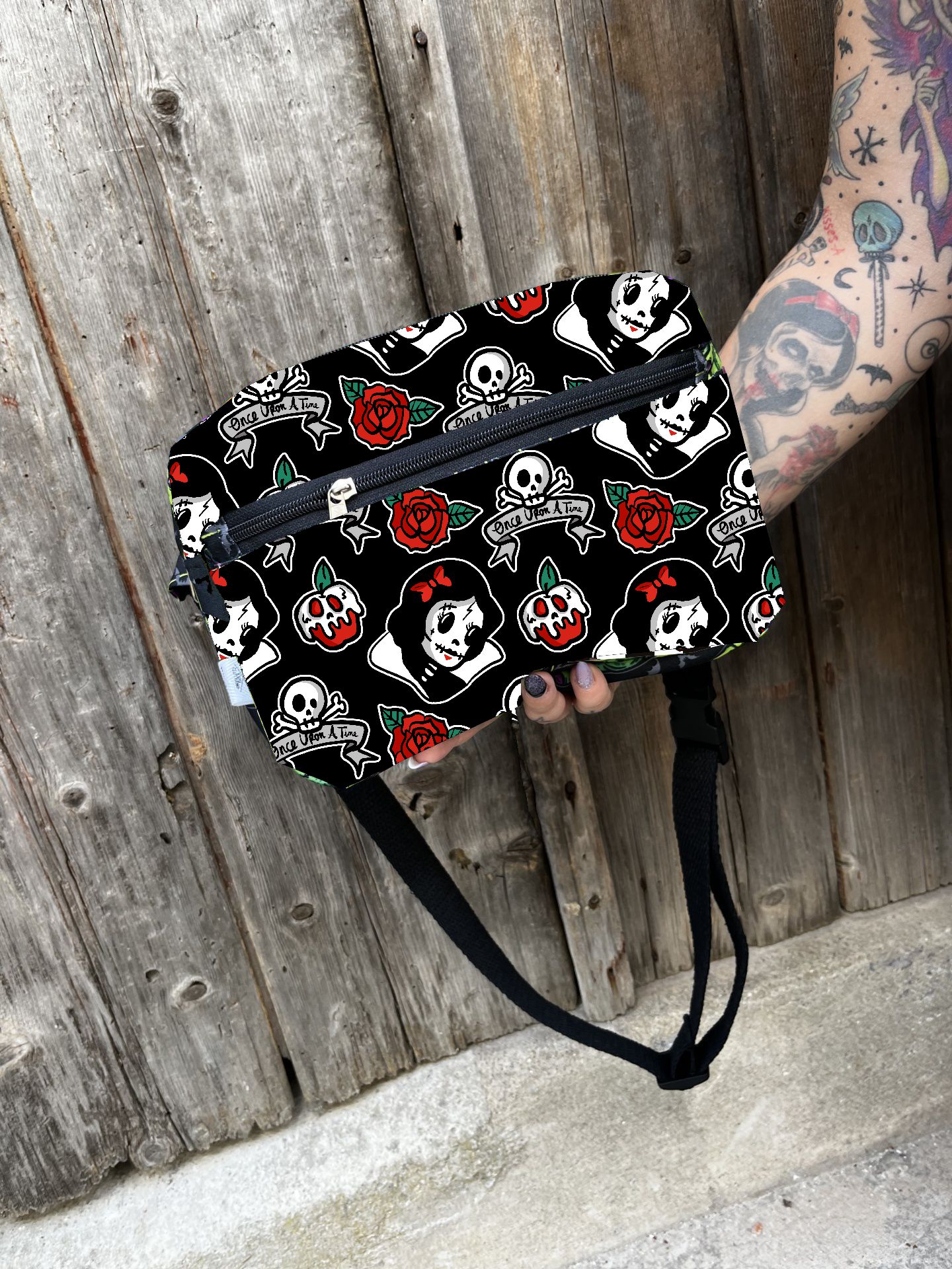 Bolsa preta com padrão de caveiras, rosas e personagens femininas estilizadas em fundo de madeira rústica