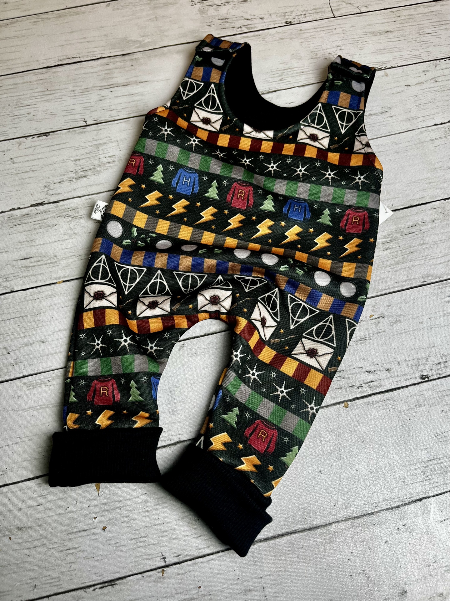 Macacão de bebé com padrão de símbolos de Harry Potter em tecido colorido.