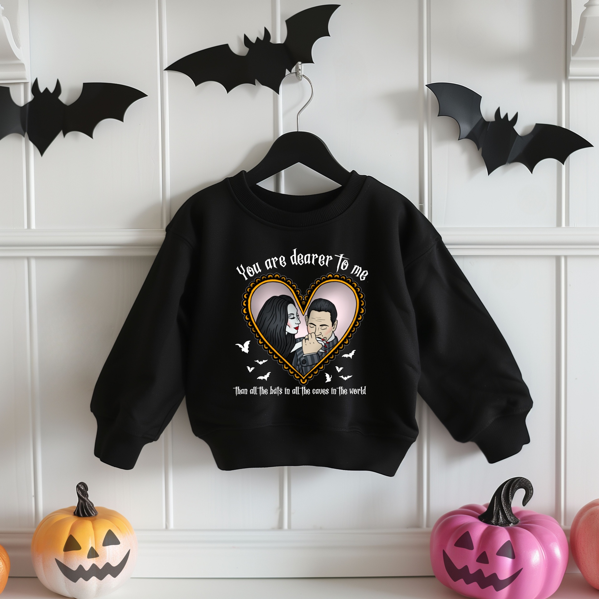 Sweatshirt preta com desenho de casal em coração e morcegos pendurada na parede com decoração de Halloween.