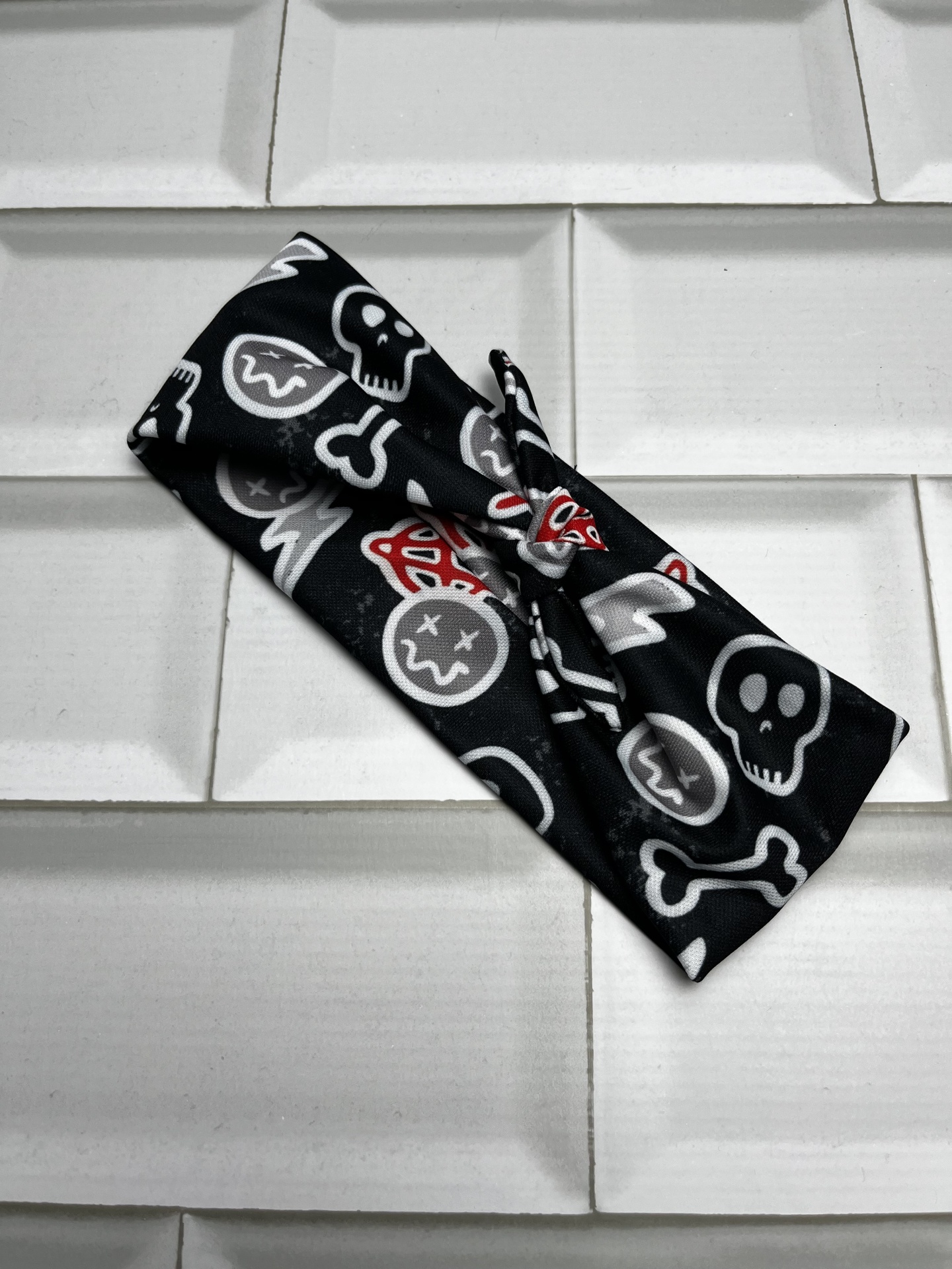 Faixa de cabelo preta com padrão de caveiras e ossos sobre azulejos brancos