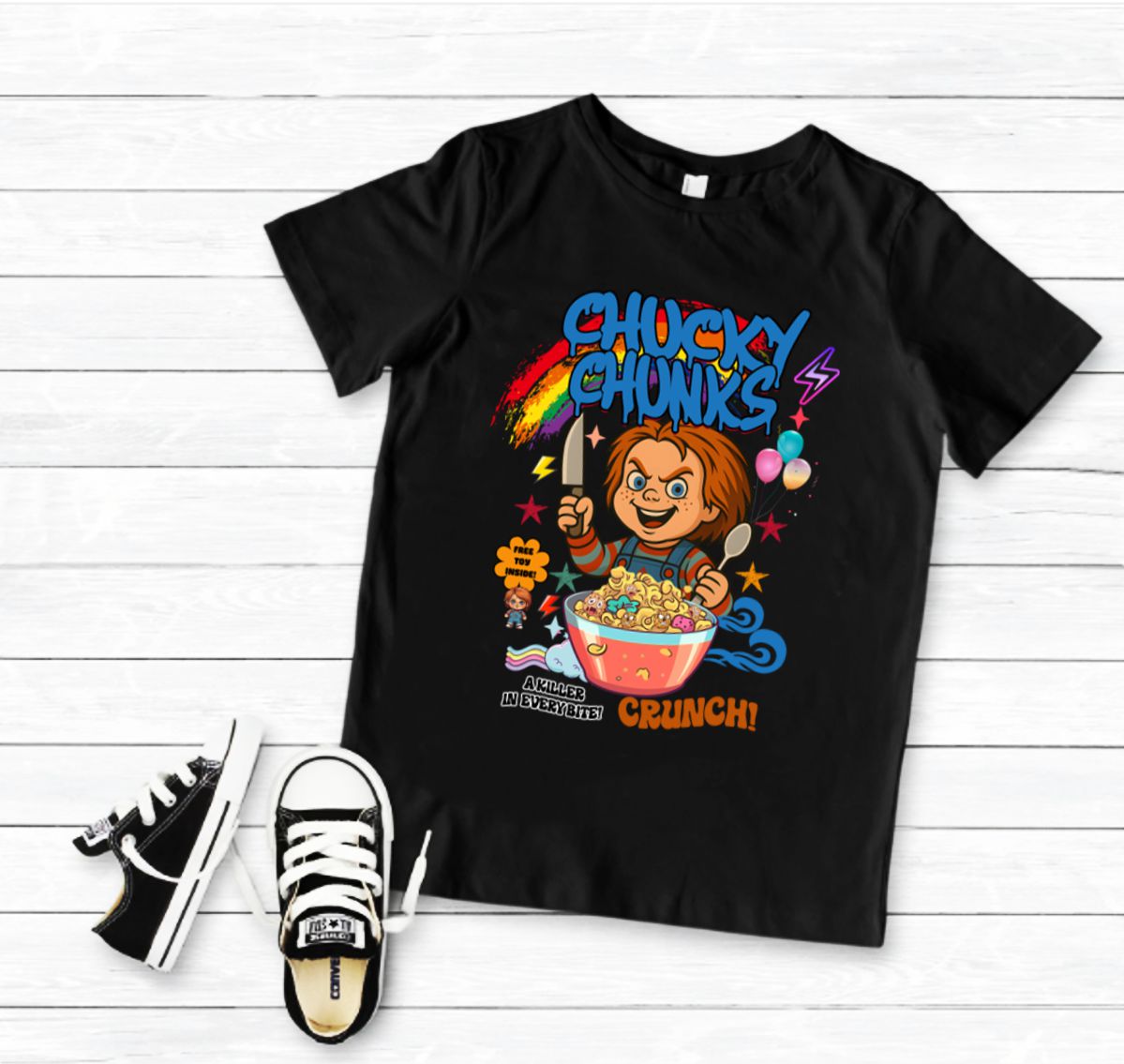 Camiseta preta infantil com estampa colorida de Chucky e ténis pretos e brancos sobre madeira branca