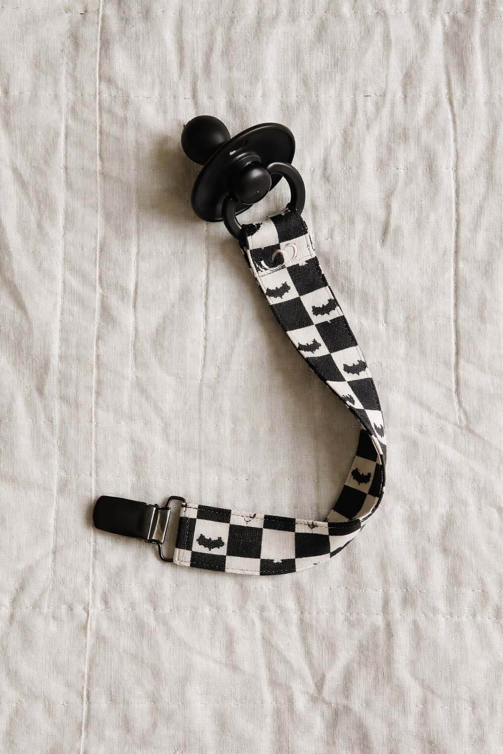 Chupeta preta com fita preta e branca aos quadrados com morcegos e prende de metal