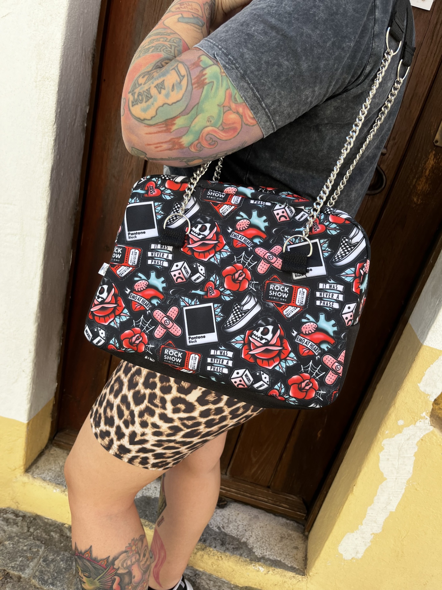 Mala preta com padrão colorido rock usada por pessoa com tatuagens e roupa casual