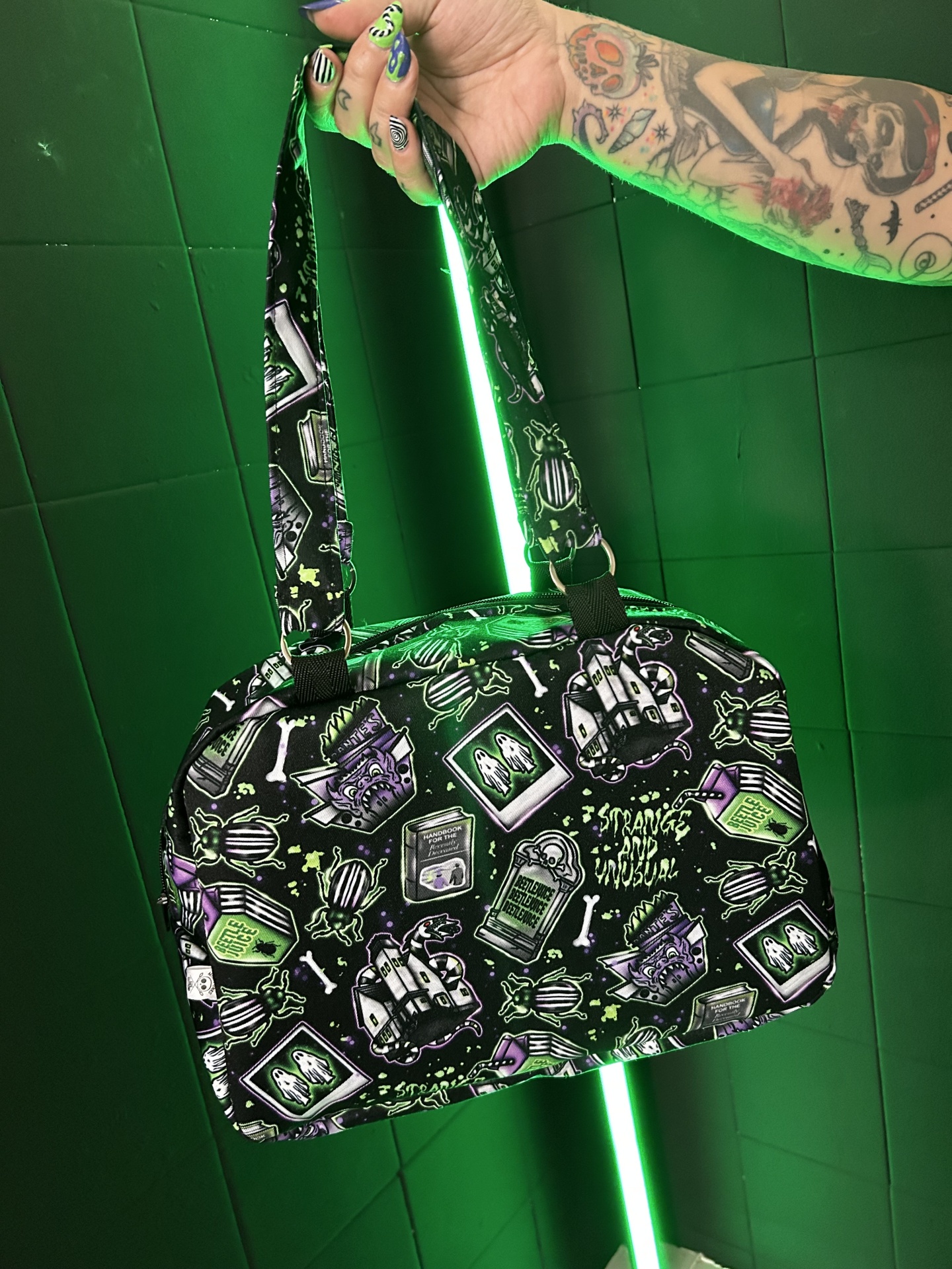 Bolsa preta com padrão colorido de desenhos místicos e de terror segura por mão tatuada