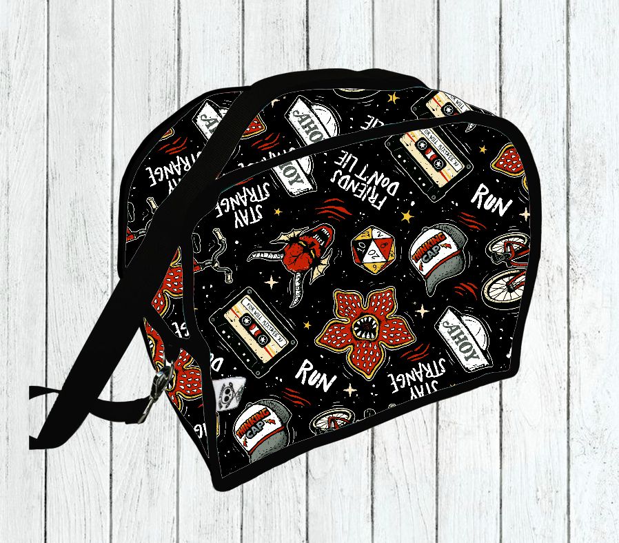 Mala preta com padrão colorido e textos vários sobre fundo de madeira branca.