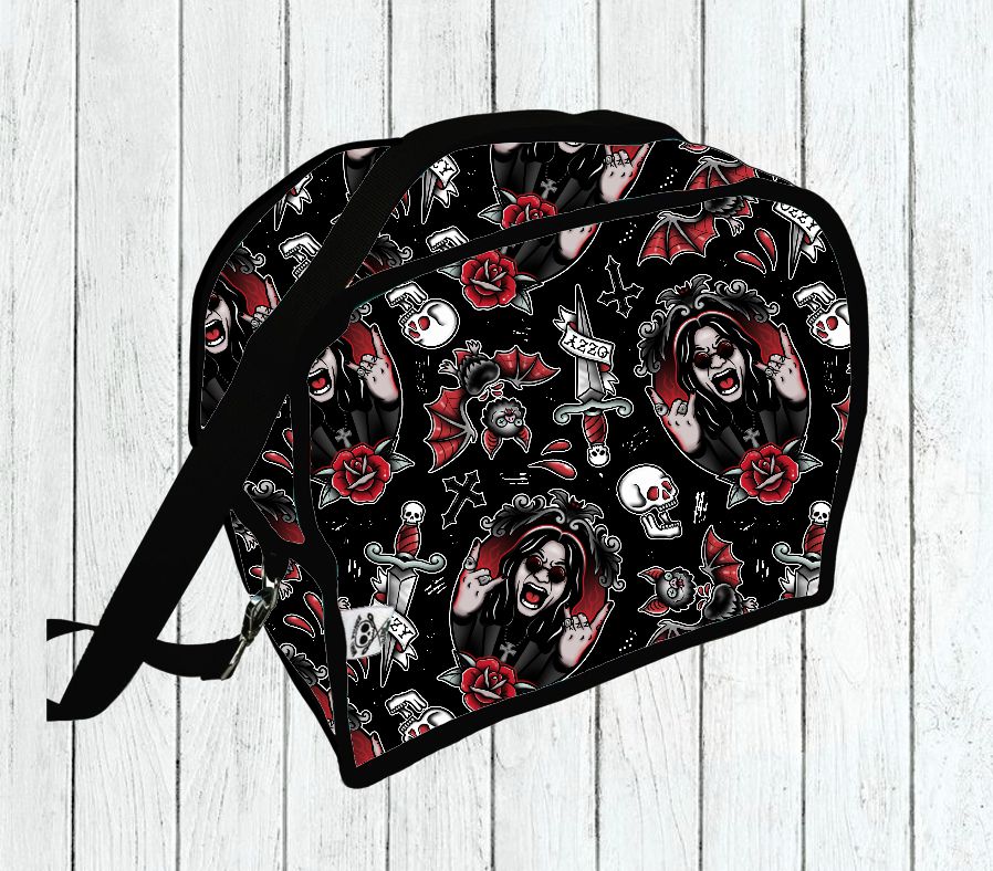 Mochila pequena preta com padrão de caveiras, morcegos, rosas e figura de mulher em fundo de madeira clara