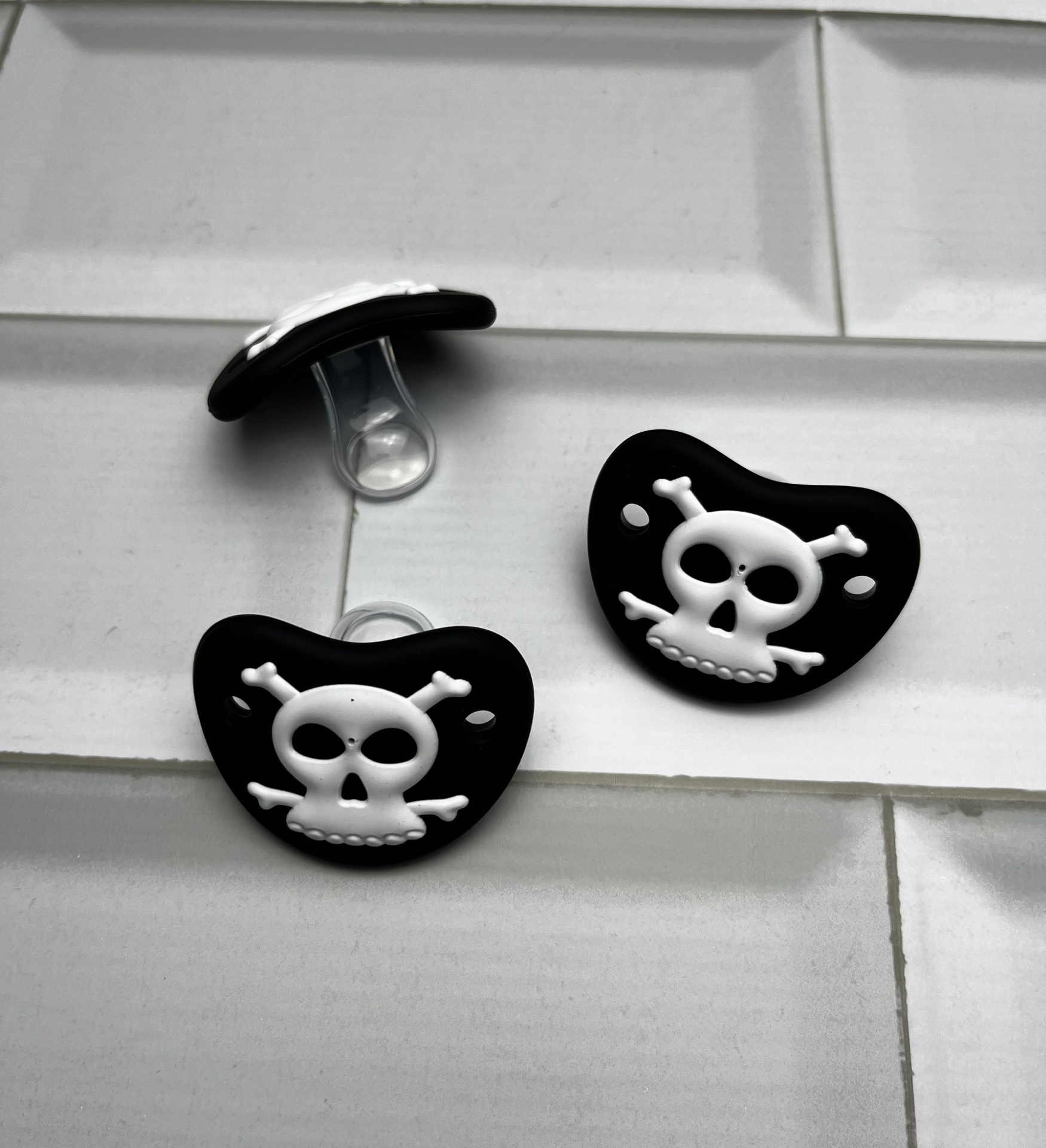 Três chuchas de bebé pretas com caveira branca