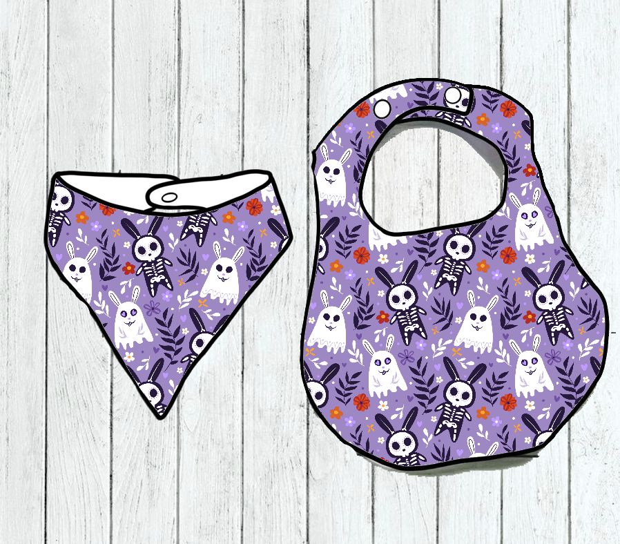 Babete e bandana roxos com padrão de esqueletos, fantasmas e folhas sobre fundo de madeira