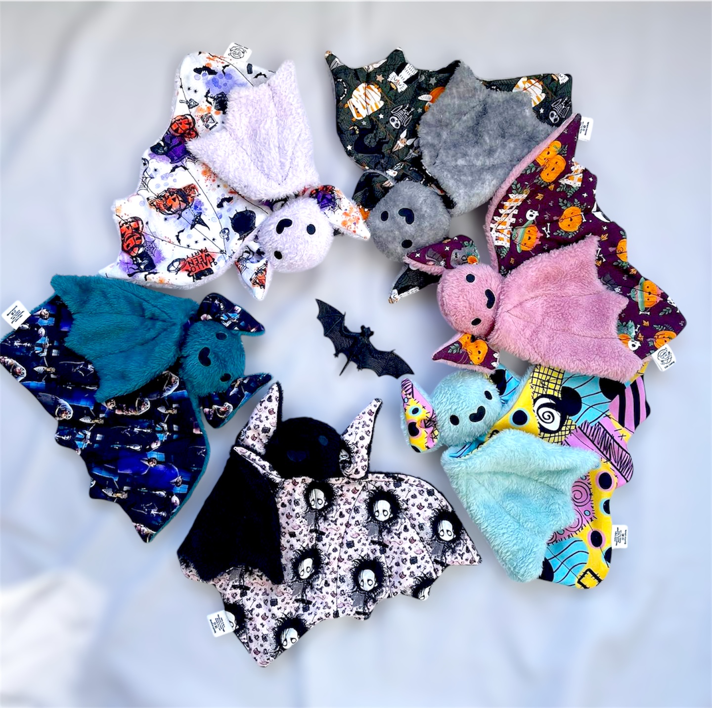 Bonecos de morcego de pelúcia coloridos com diferentes padrões e um morcego preto de plástico no centro.