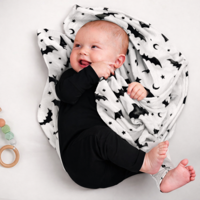 Bebé com macacão preto deitado em manta branca com padrão de morcegos e estrela