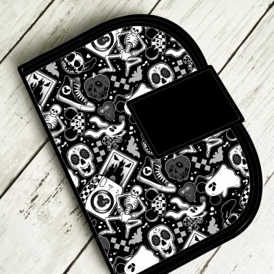 Bolsa preta com padrão de esqueletos e caveiras em preto e branco com aba preta sobre piso de madeira claro