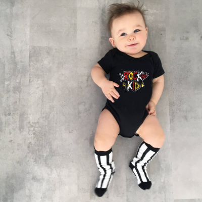 Bebé com body preto e meias pretas e brancas deitado em chão cinzento.