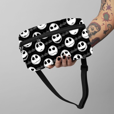 Bolsa tipo cintura preta com padrão de rostos brancos e fecho de correr preto, segurada por mão com unhas pretas e braço tatuado.