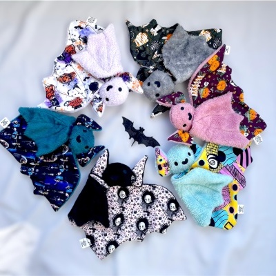 Bonecos de morcego de pelúcia coloridos com diferentes padrões e um morcego preto de plástico no centro.