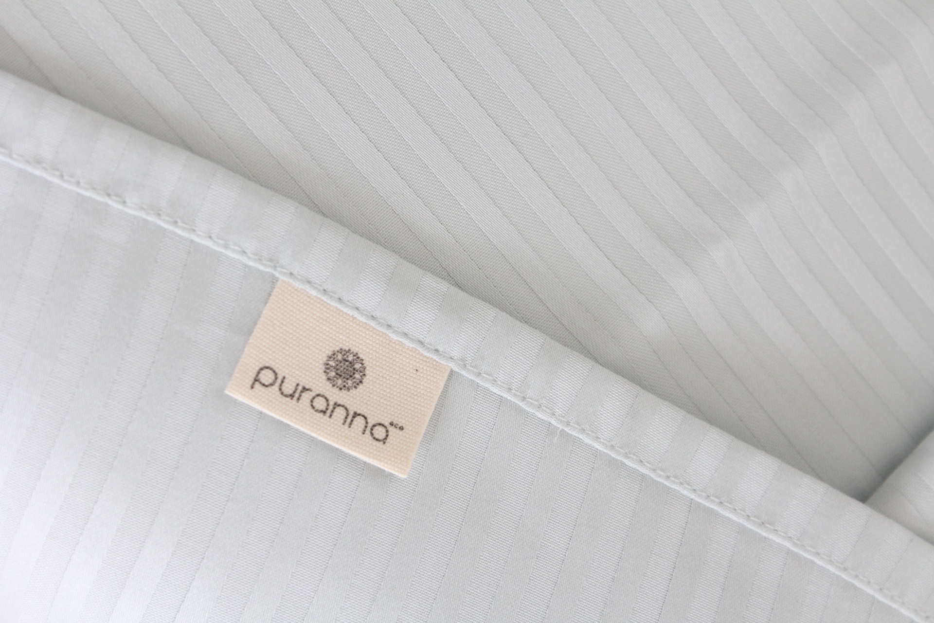 Pano branco com etiqueta da marca puranna e padrão riscado